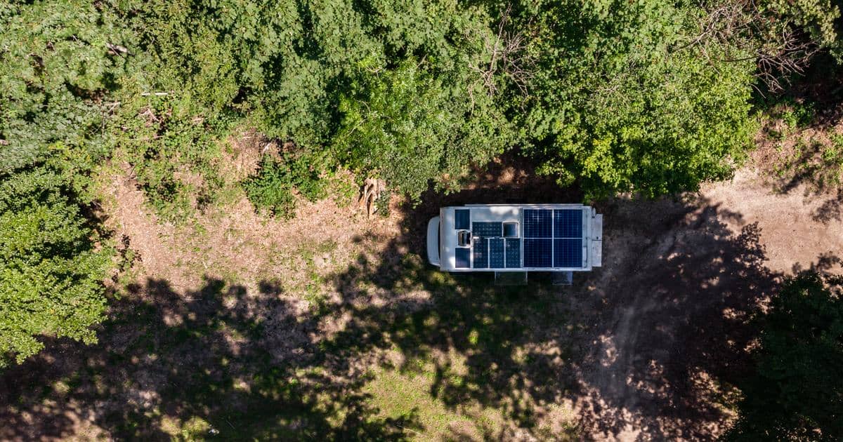Vedere aeriană a unei autorulote cu panouri solare pe acoperiș, parcată într-o poiană din pădure