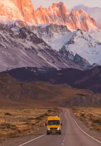 Autorulotă galbenă pe un drum deschis, sub masivul înzăpezit Fitz Roy din Patagonia
